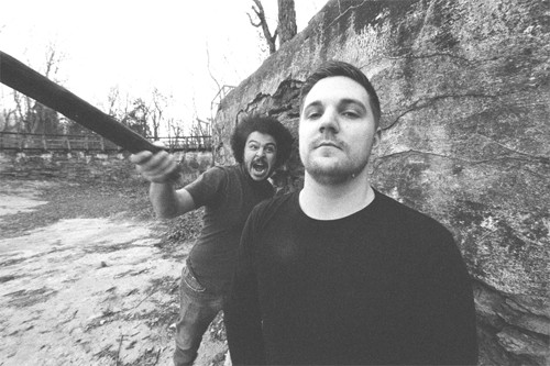 Black-and-white photo of the two members of Buz outdoors beside a rock wall